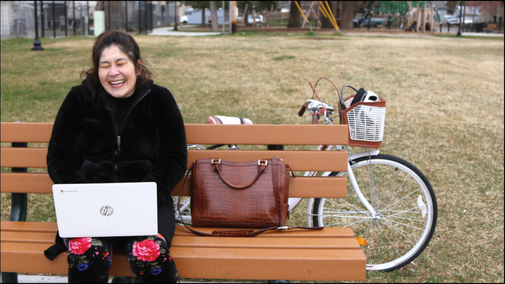 Woman using laptop laughing joyfully with bicycle in background.