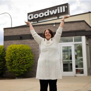 Woman standing outside a building holding up a Goodwill sign.