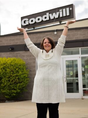 Woman standing outside a building holding up a Goodwill sign.
