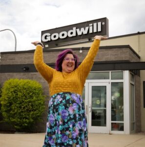 Woman standing outside a building holding up a Goodwill sign.