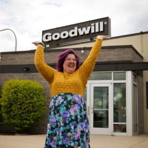 Woman standing outside a building holding up a Goodwill sign.