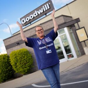 Woman standing outside a building holding up a Goodwill sign.