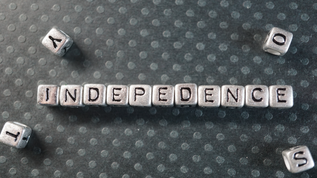 A group of square beads with letters on them are lined together and spell out the word "independence".