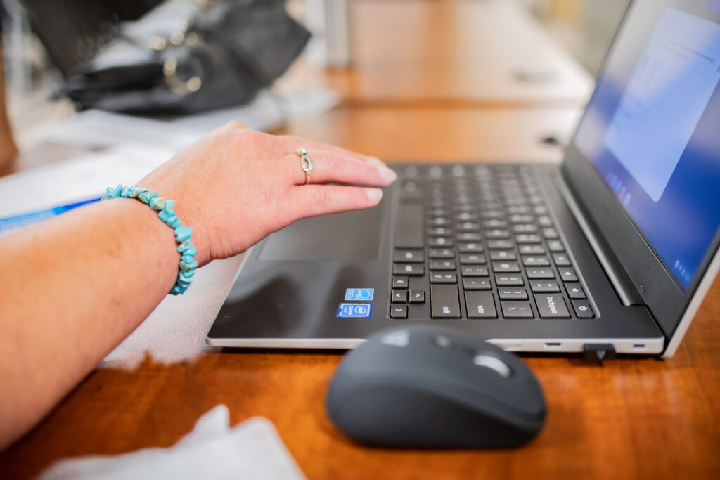 A woman's hand is hovering over the keyboard of a laptop computer. A computer mouse sits nearby.