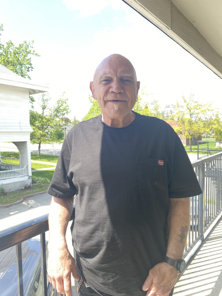 An elderly man is standing on a second level of an apartment building, outside.