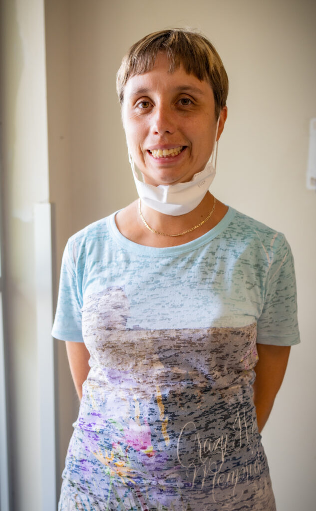 A woman with a mask pulled below her chin is smiling at the camera.