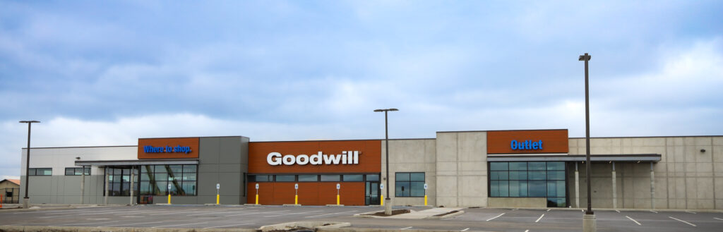 long building with signs attached to the front. Where to shop is written in blue on the left hand side. Goodwill is written in white in the center. Outlet is written in blue on the left hand side.
