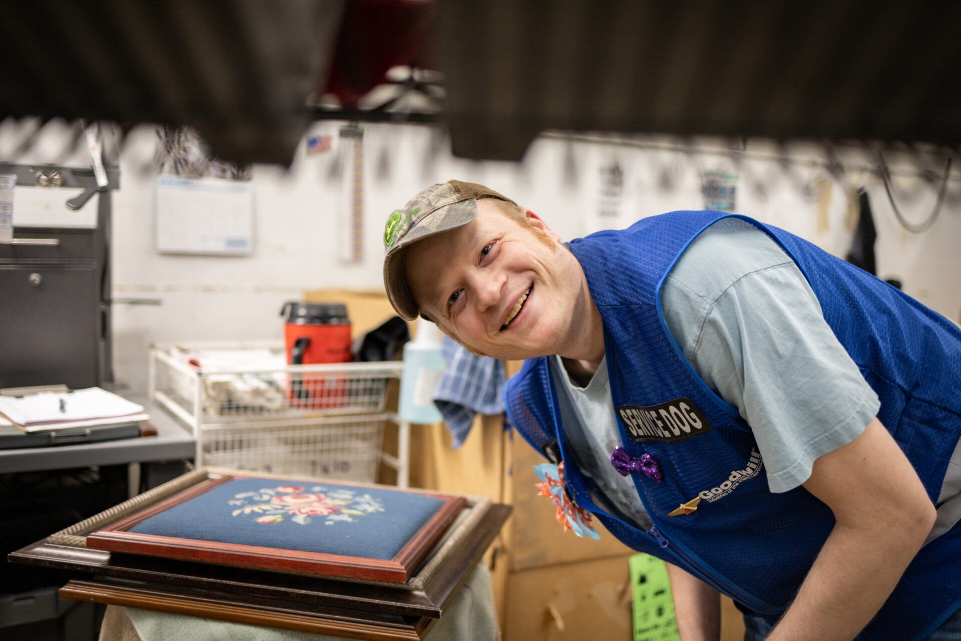 A man wearing a blue vest is leaning below a shelving unit and smiling between the shelves.