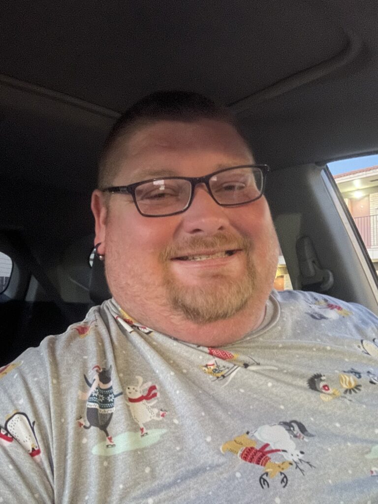 A selfie of a man wearing glasses and sitting in a car, smiling.