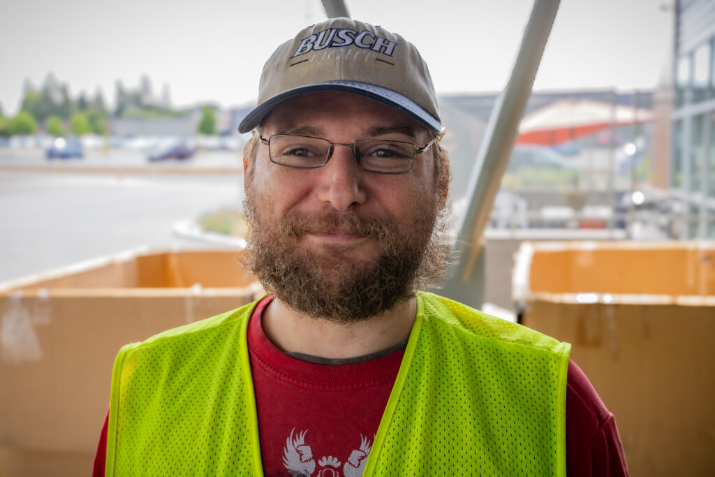 A man wearing a high visibility yellow vest is standing outside of a donation center, smiling.