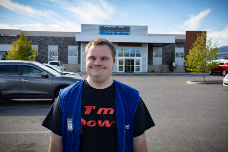 A man wearing a blue vest is standing outside in a parking lot with a Goodwill store behind him.