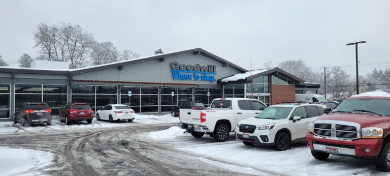 Coeur d'Alene, Idaho Goodwill front of store with the parking lot covered in snow and cars parked in parking lot.