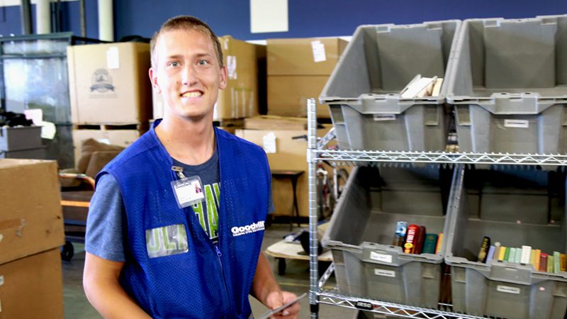 Goodwill employee standing in front of bins of books.