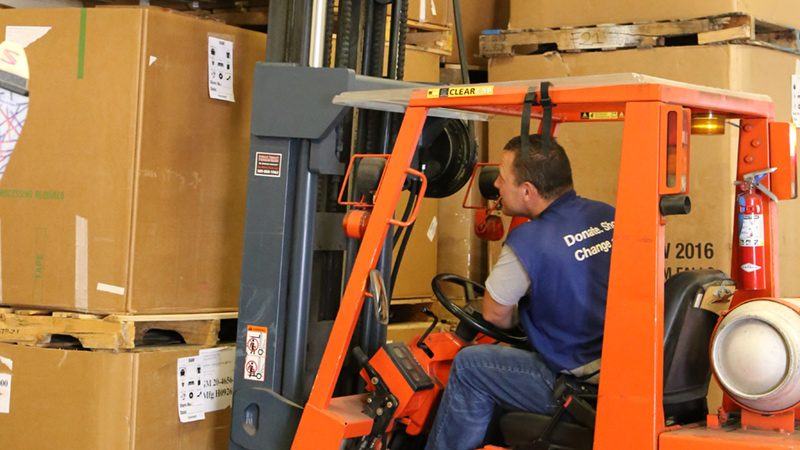 Man using forklift to move large cardboard boxes.